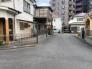 前面道路含む現地写真　旧開発現場内に位置し、車通りが少なく静かな住環境が保たれた落ち着いた立地。ご夫婦でゆっくりと散歩を楽しむ、そんな穏やかな日常の風景がこの場所には広がっています。