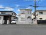 前面道路含む現地写真　白い外観と玄関まわりを正面から撮影しています。道路との距離や駐車スペースの位置関係を写真で確認し、建物の印象や出入りのしやすさを現地内覧でお確かめください。玄関前の様子も現地であわせてご確認ください。